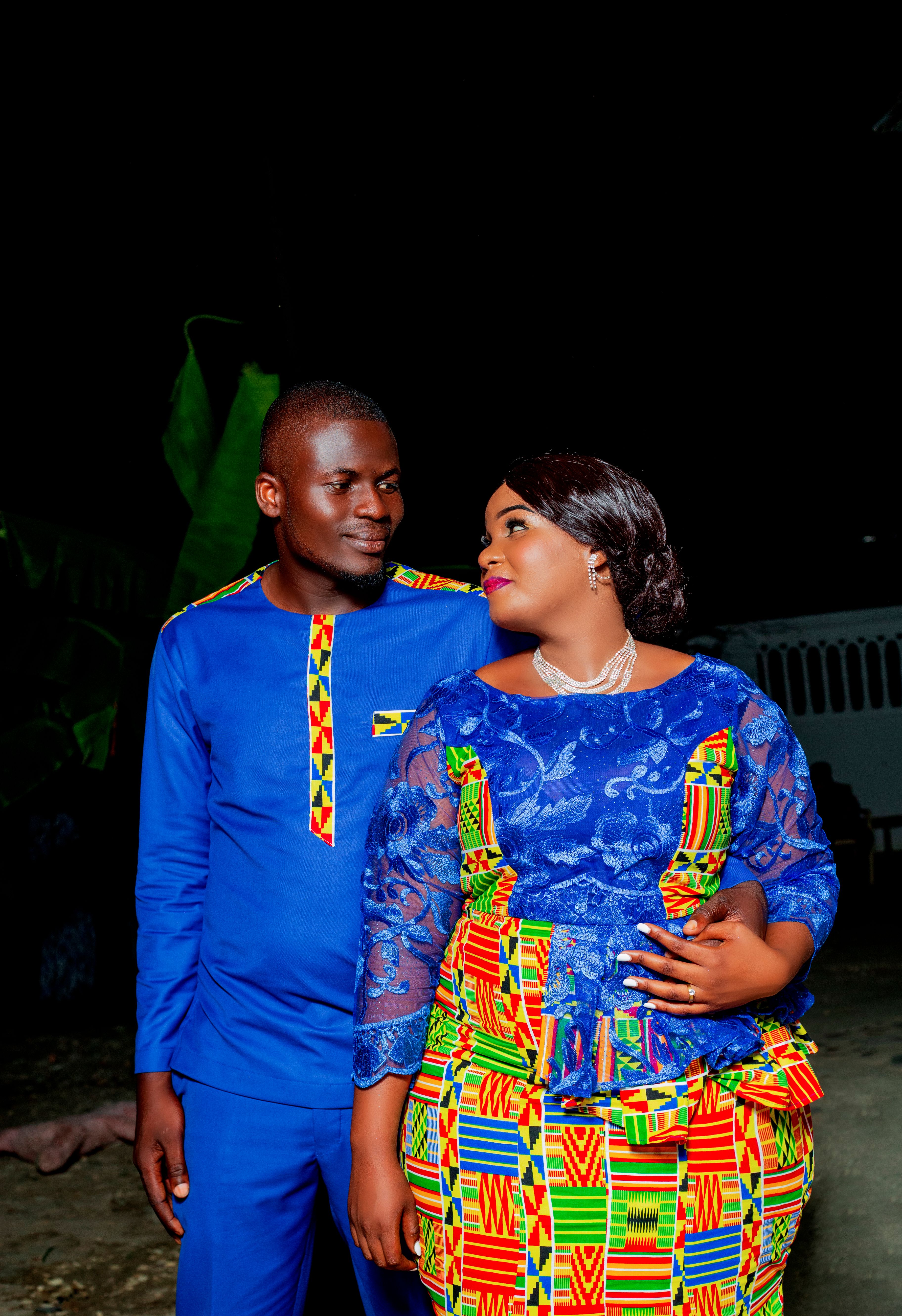 Couple in colorful traditional attire smiling together outdoors at night.
