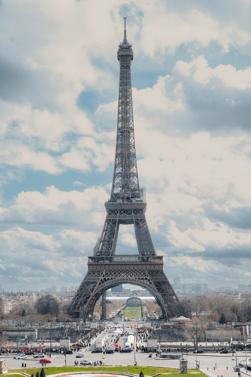 Free Iconic Eiffel Tower with a bustling Paris crowd beneath a partly cloudy sky, capturing urban charm. Stock Photo
