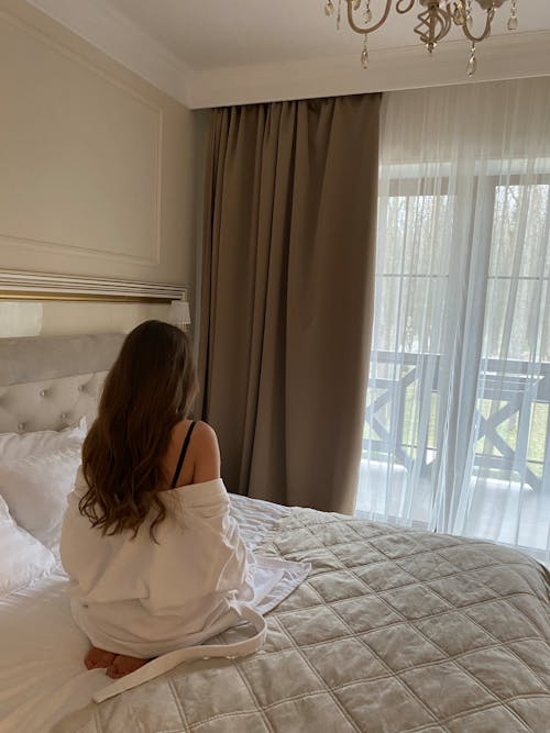 Free Woman Sitting on the Bed Looking out the Window Stock Photo
