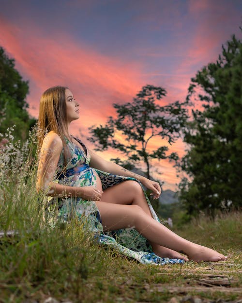 Portrait of a Pregnant Brunette Sitting on the Grass at Dusk