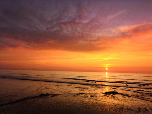 Free A stunning sunset casts vibrant colors over a serene beach and ocean waves. Stock Photo