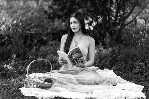 Young Woman Sitting on a Blanket in a Park and Reading a Book 