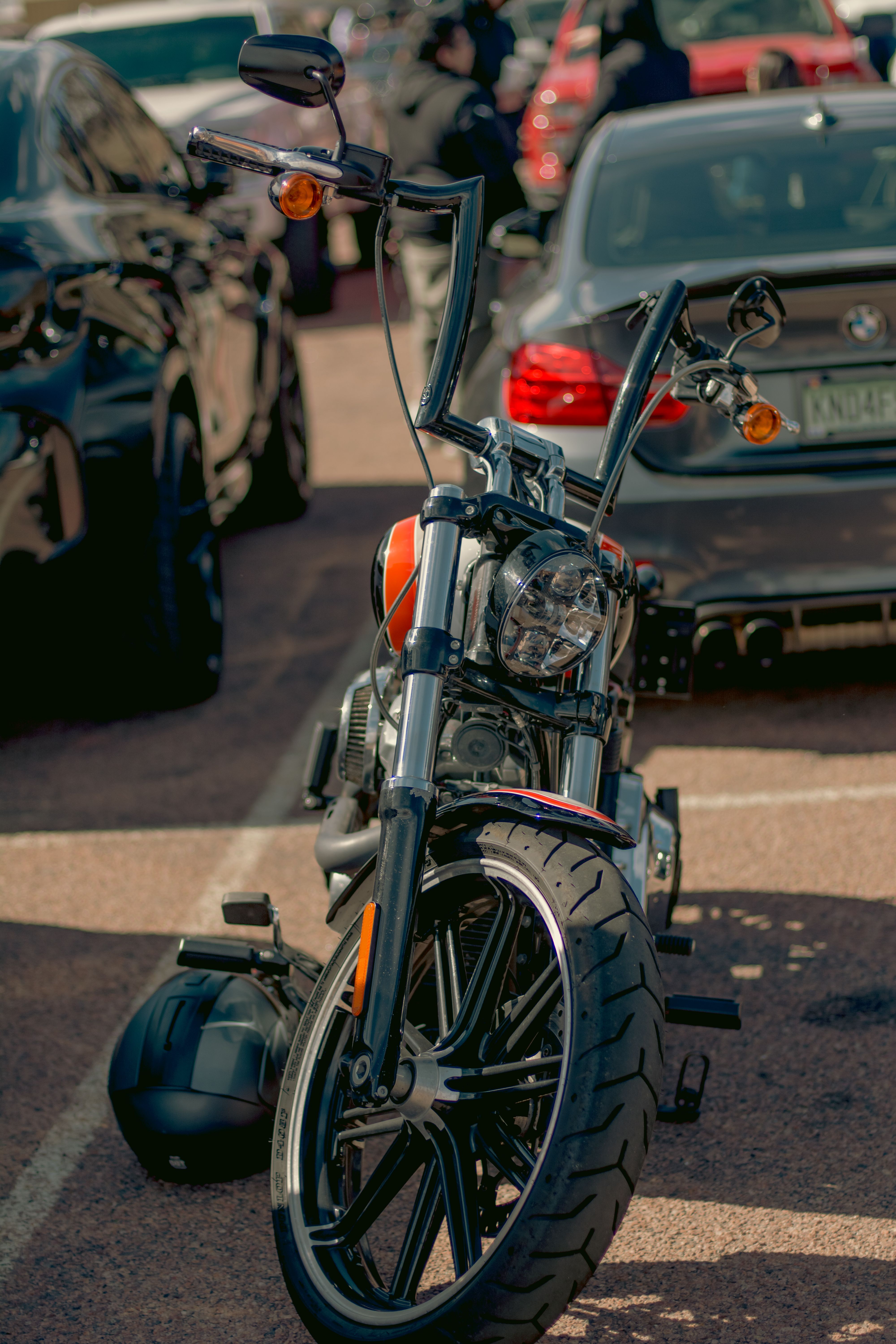 Close-up of a motorcycle parked among cars in a city parking lot during the day.