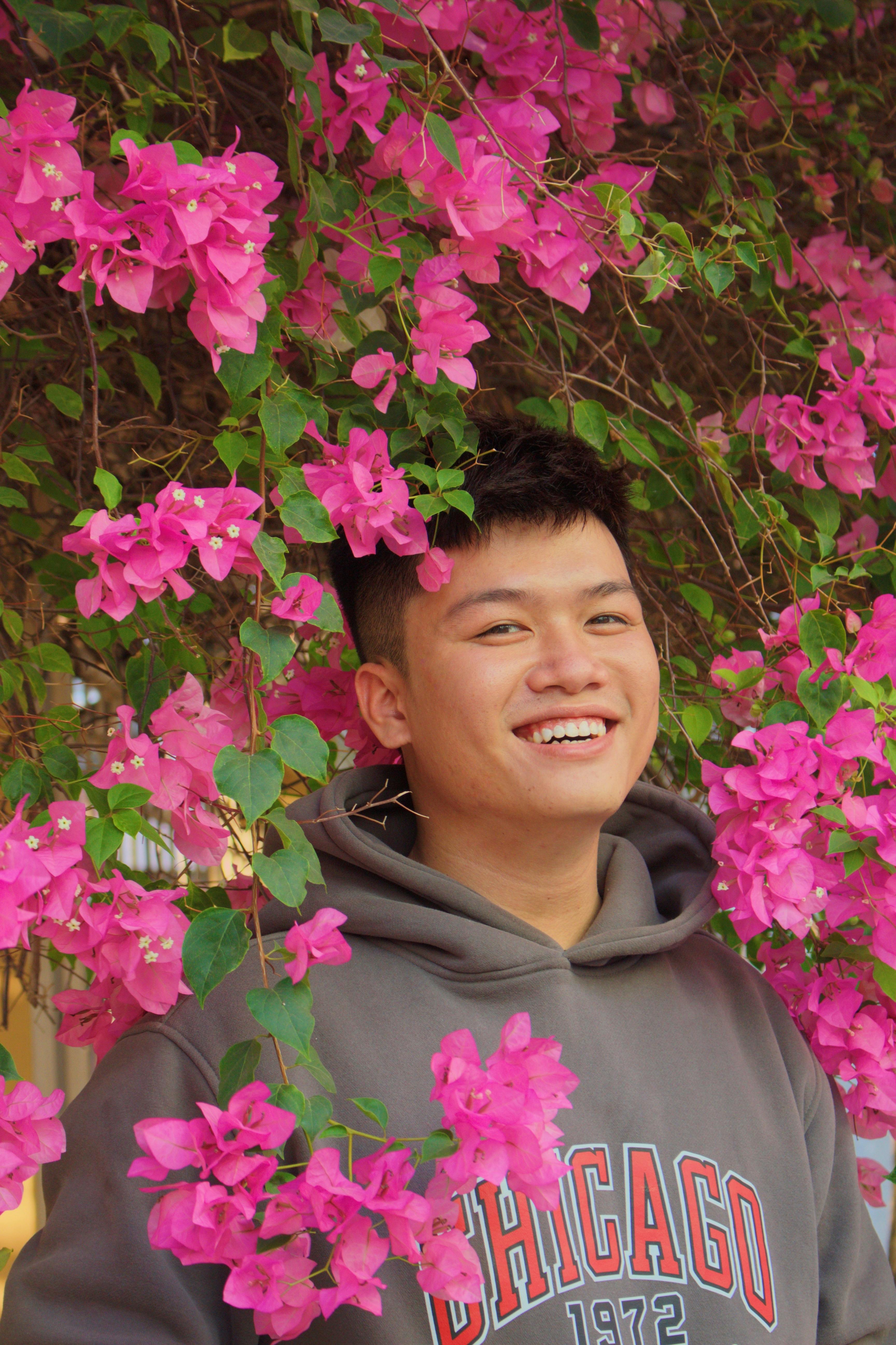 Joyful man in a garden surrounded by vibrant pink flowers, wearing a hoodie.