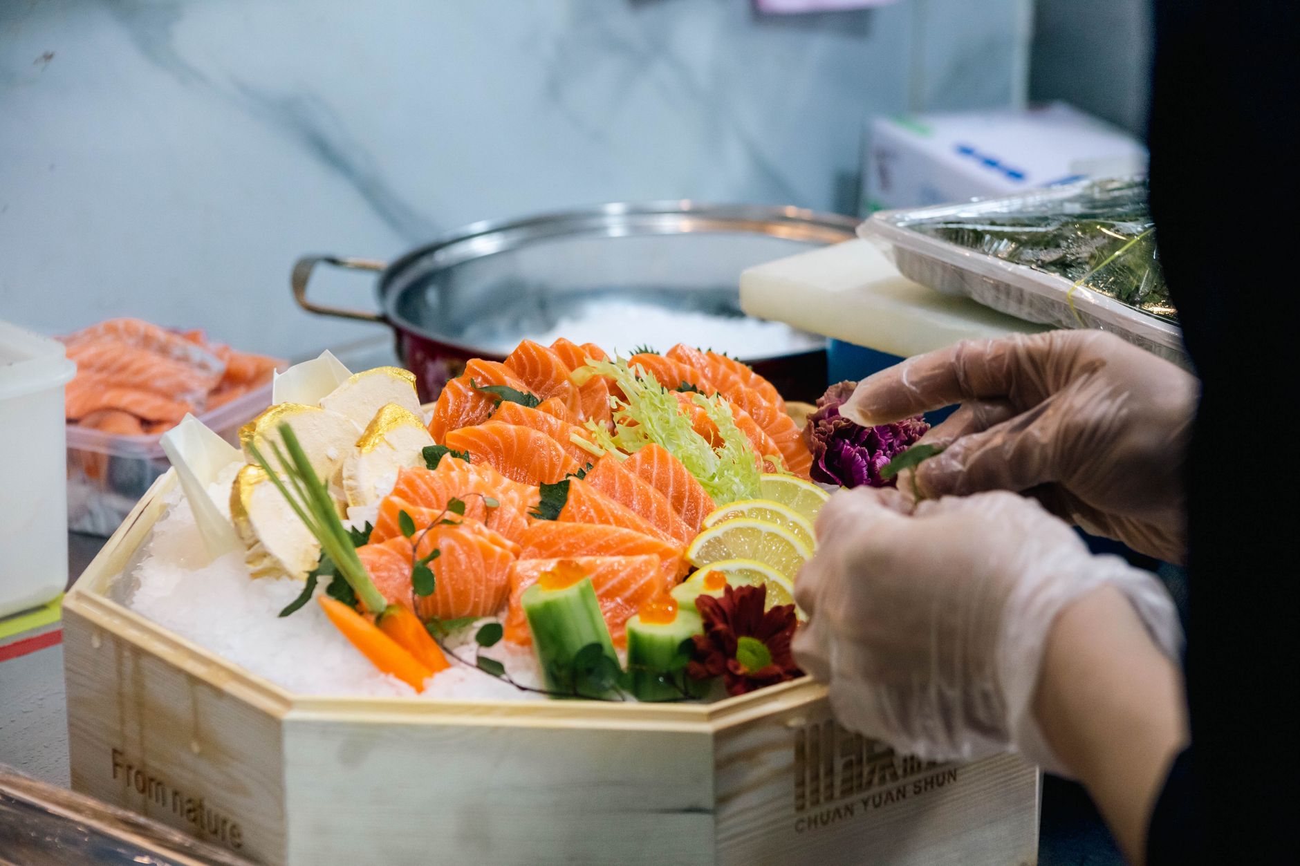 Chef arranging colorful salmon sashimi platter with vegetables in a professional kitchen.