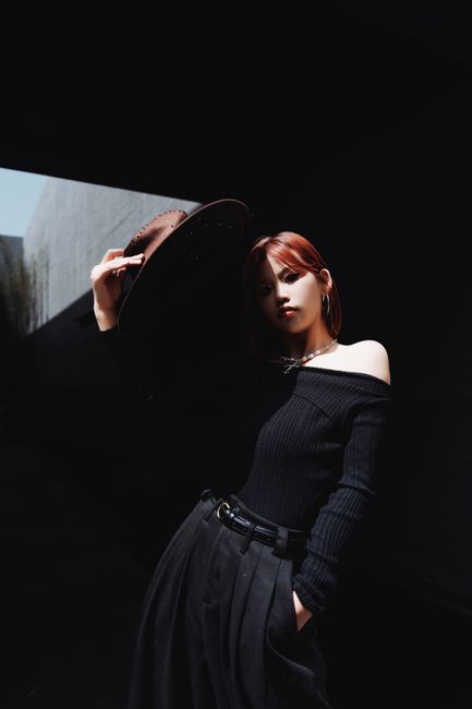 Fashionable young woman posing in a black outfit with dramatic shadows.