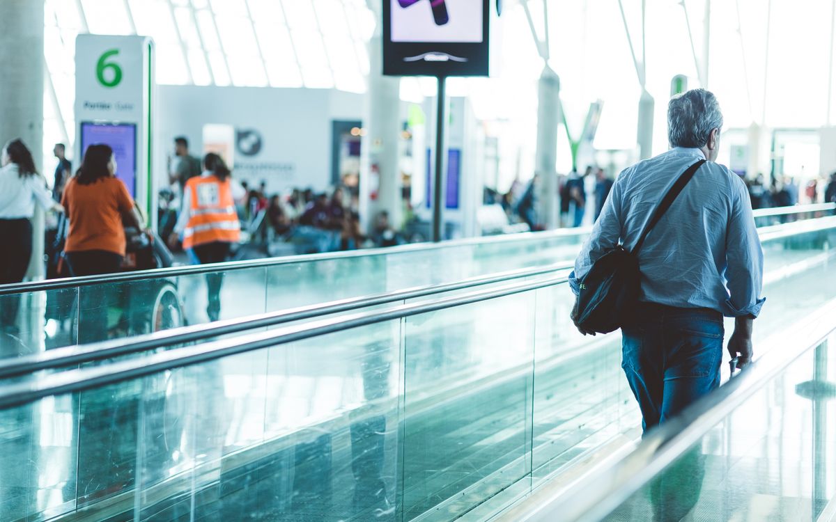 A bustling airport scene with travelers on a moving walkway in a modern terminal.