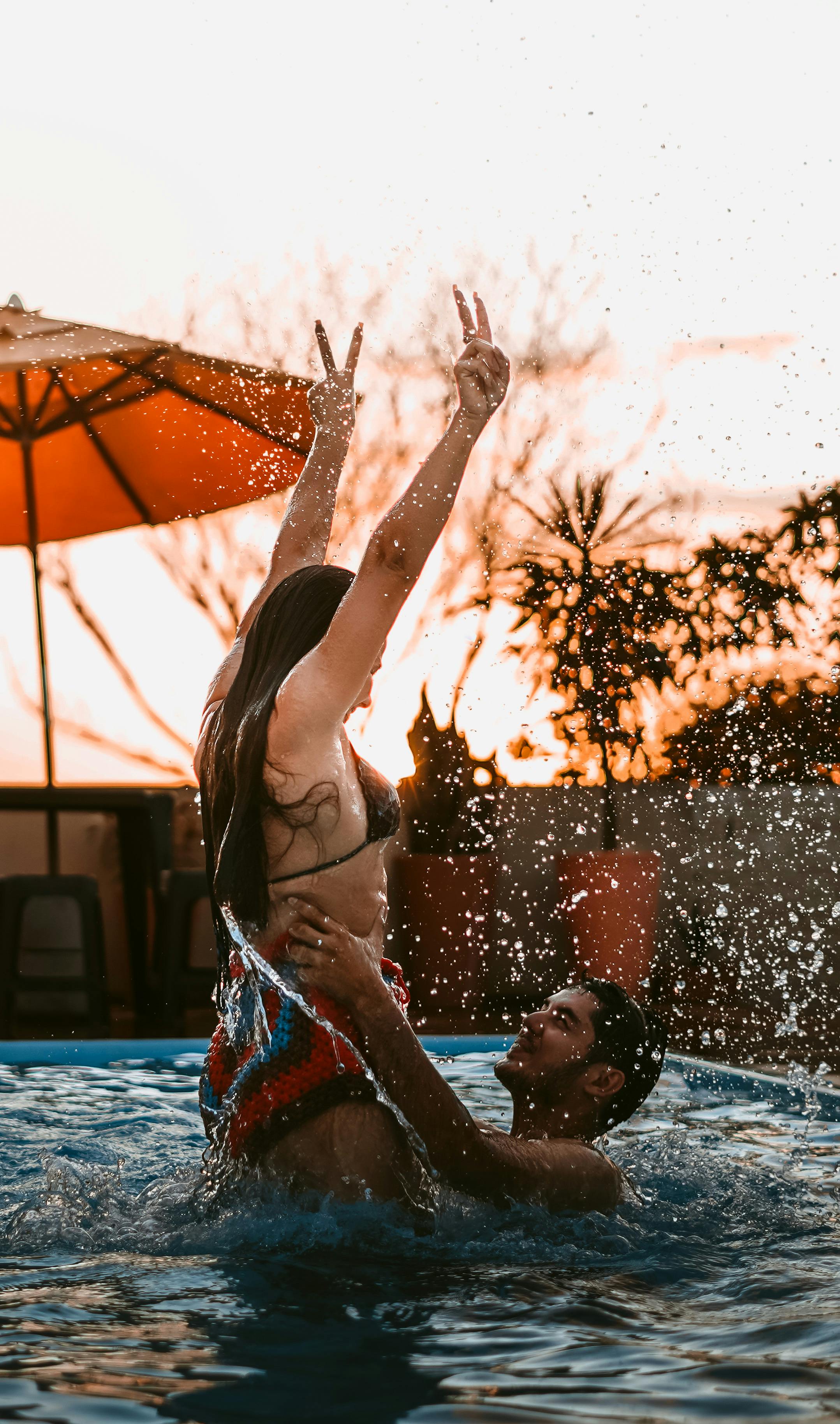 A joyful couple having fun in a pool during sunset, splashing water playfully.