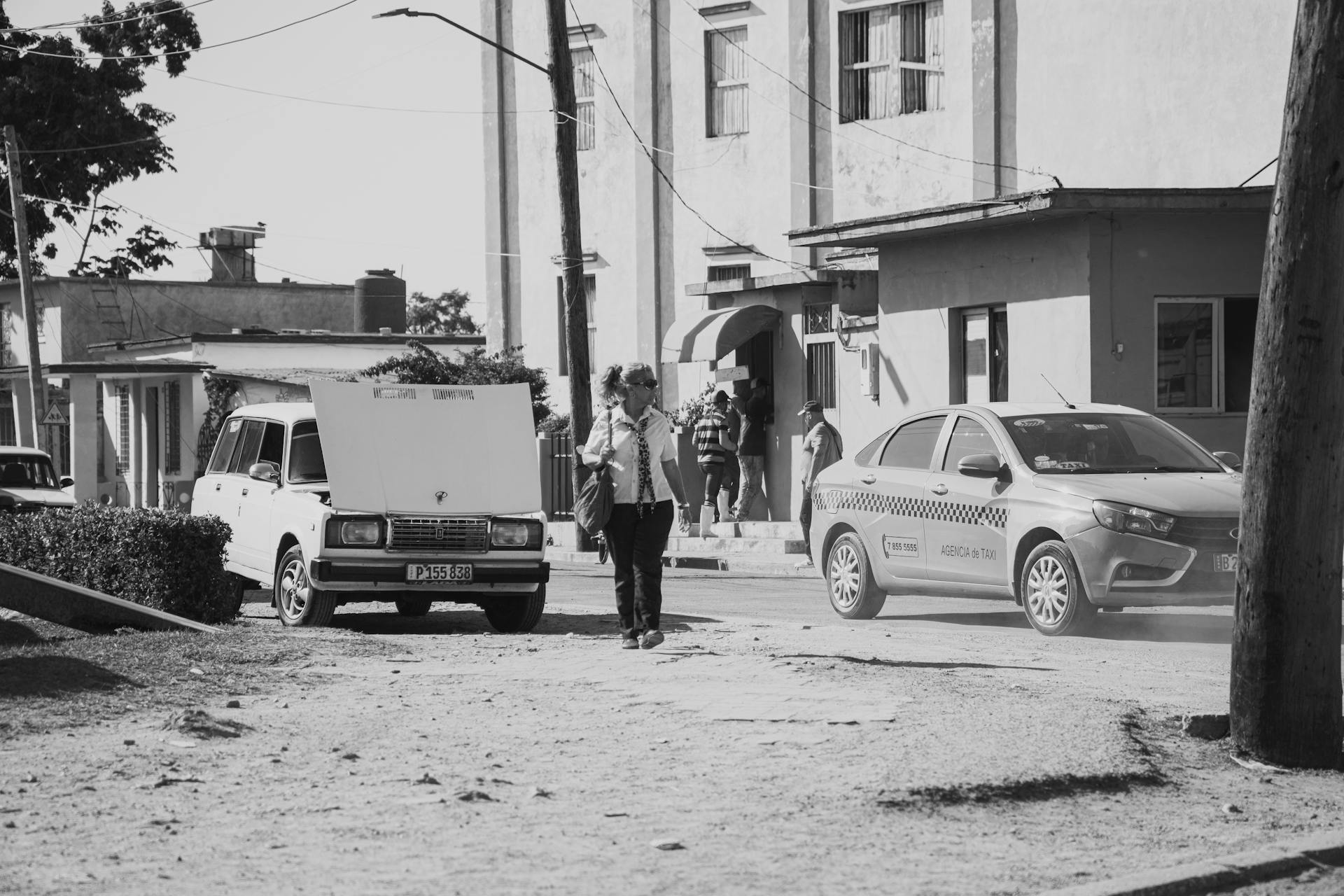 Monochrome street scene in Cuba featuring vintage cars and daily life activities.