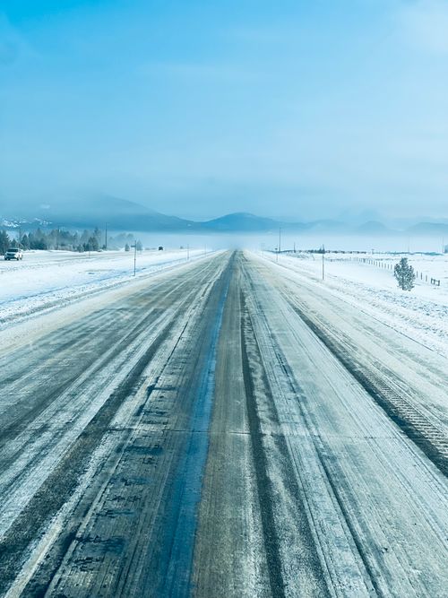 Free A mesmerizing winter scene of a snow-covered road leading into a misty mountainscape under a clear blue sky. Stock Photo