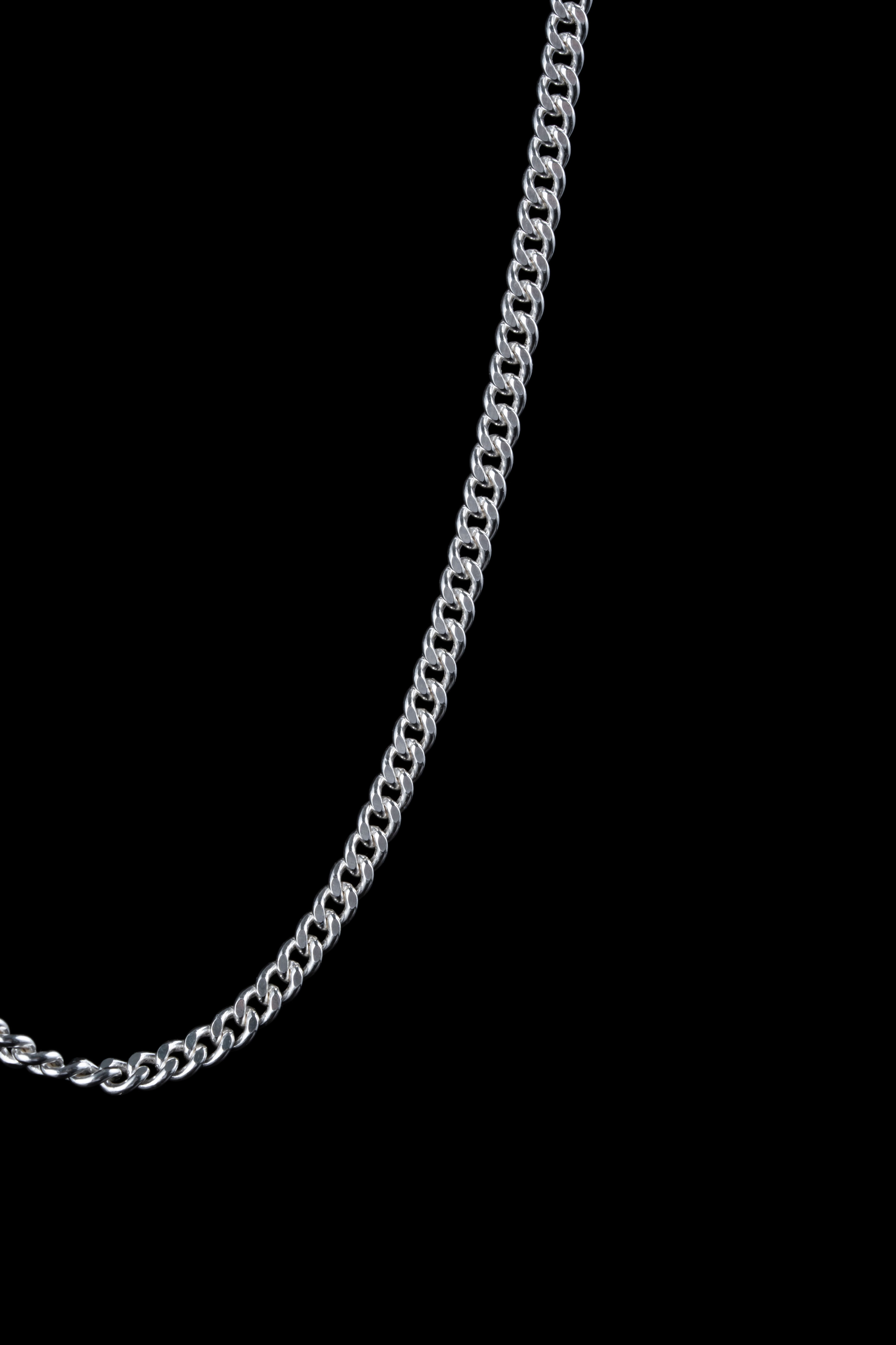 Close-up of a silver Cuban link chain, handmade jewelry highlighted against a black background.