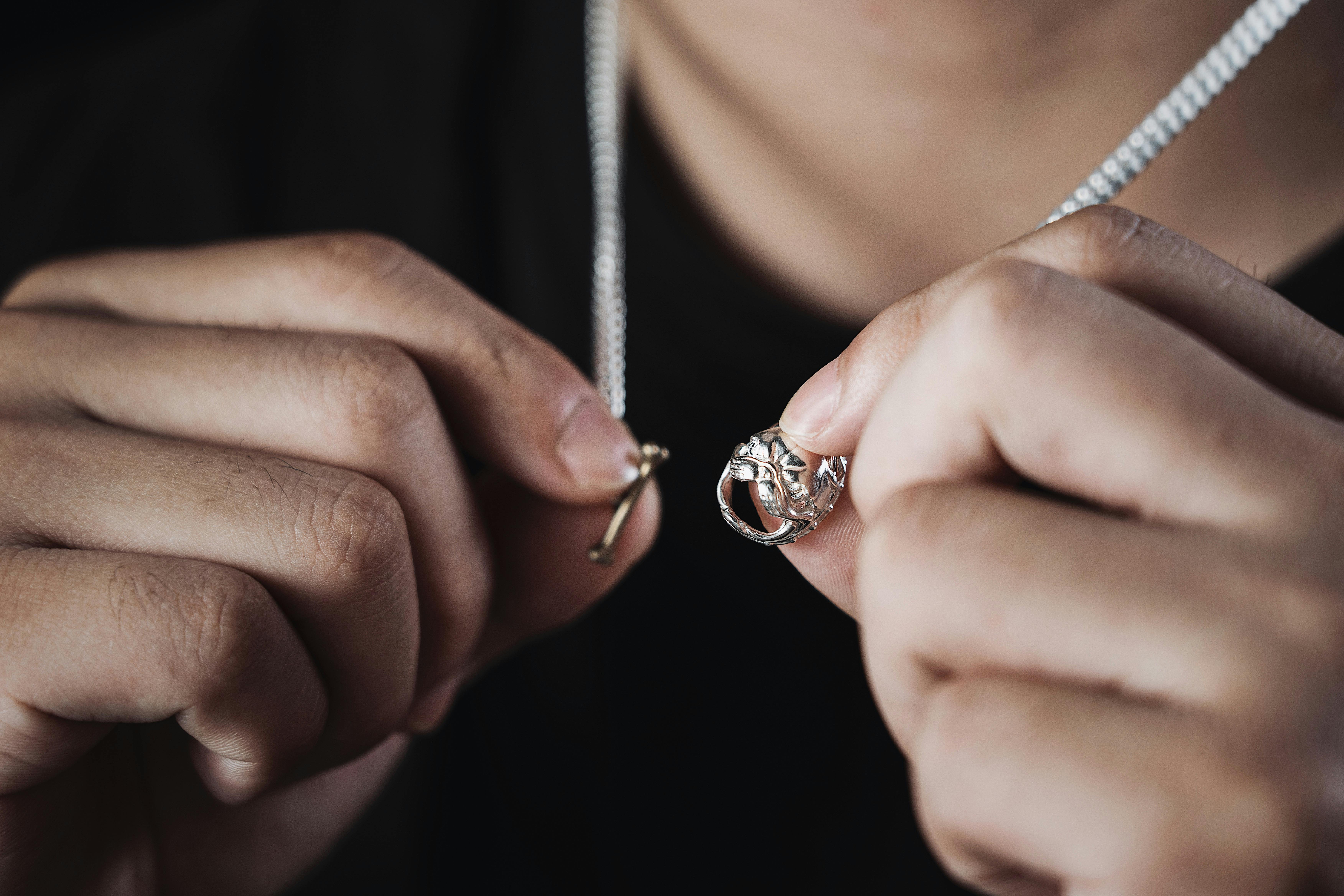 Close-up shot of a man displaying a handmade silver necklace with a pendant.