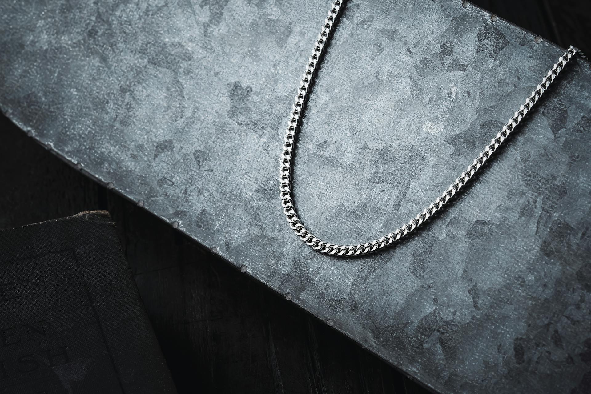 A stylish silver Cuban link chain displayed on a textured dark surface, highlighting its intricate design.