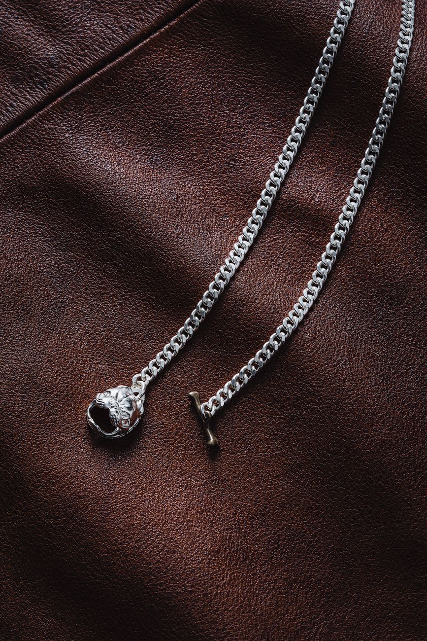 Close-up of a silver chain necklace on textured leather, showcasing intricate pendant design.