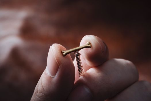 A close-up view of a hand holding a gold bone-shaped pendant against a blurred background.