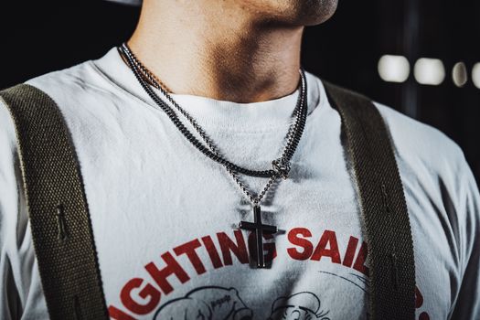 Close-up of a man wearing a cross necklace and graphic T-shirt, showcasing trendy jewelry.