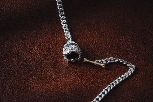 Close-up of a silver chain necklace with an animal head pendant on a textured leather surface.