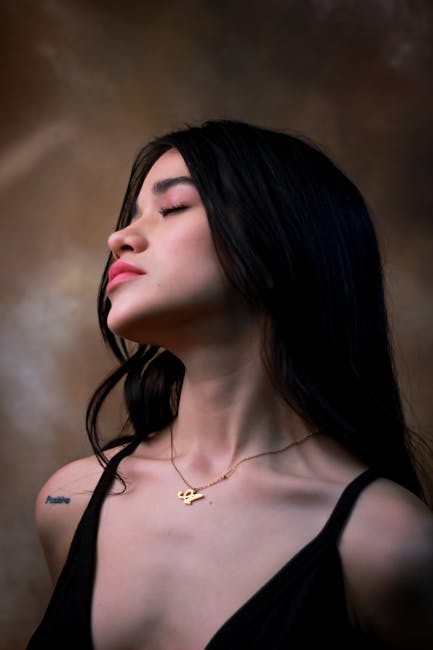 Profile portrait of a young woman with tattoos and long hair, eyes closed.