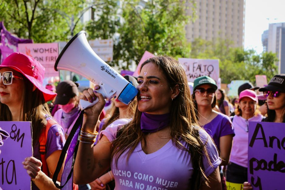 Una mujer liderando apasionadamente una protesta, hablando en un megáfono con una multitud vibrante de fondo.