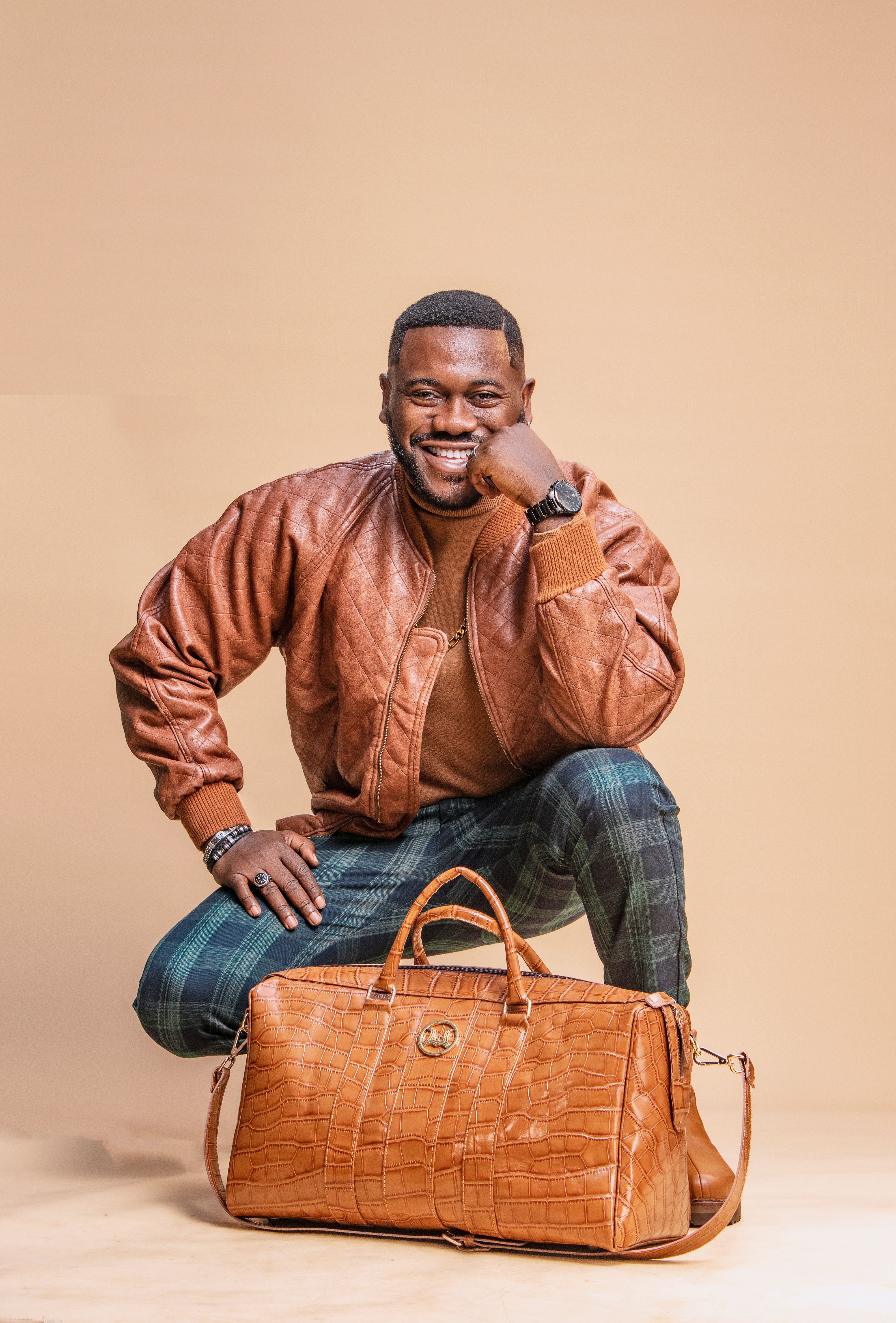 African American man in stylish leather jacket crouching with a leather bag, in a studio shot.