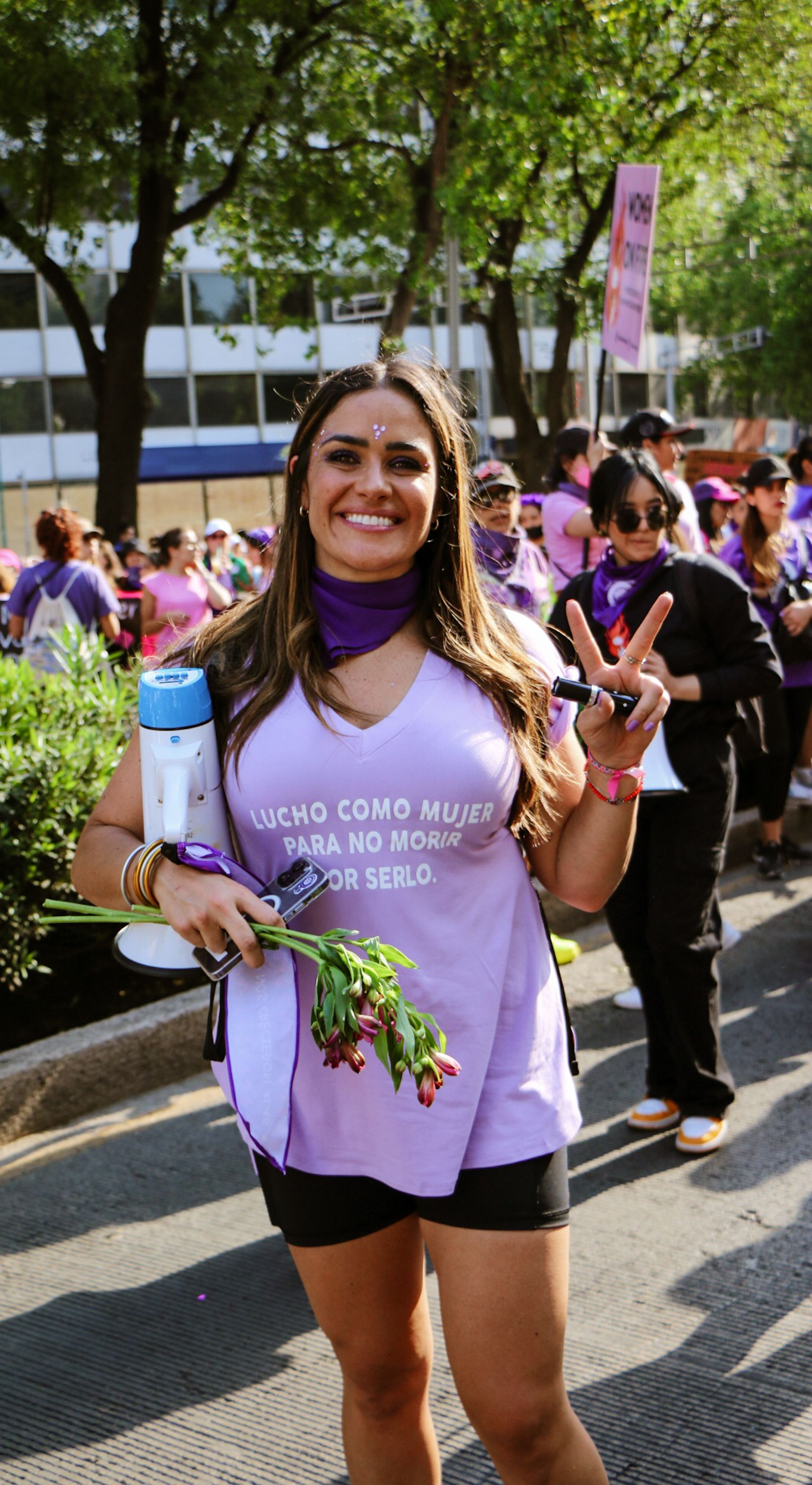 Smiling woman with flowers, peace gesture at protest rally, promoting women's rights.