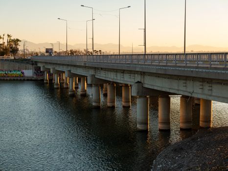 A serene view of a bridge crossing water with mountains in the background during sunset.