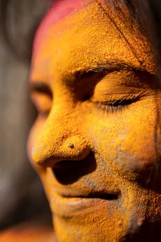 Close-up shot of a woman with closed eyes and colorful powder on her face, conveying joy and celebration.