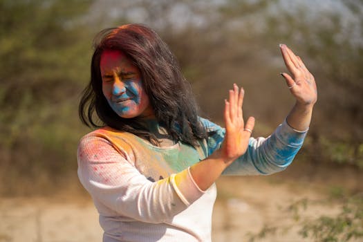 Woman enjoying Holi festival with vibrant colors on her face and clothes in an outdoor setting.