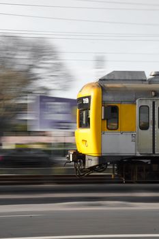 A yellow train speeds down blurred city tracks, capturing urban motion.