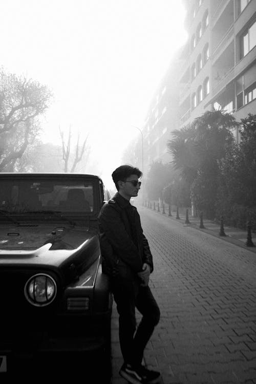 Young Man Standing Next to a Car on a Foggy Street in City 