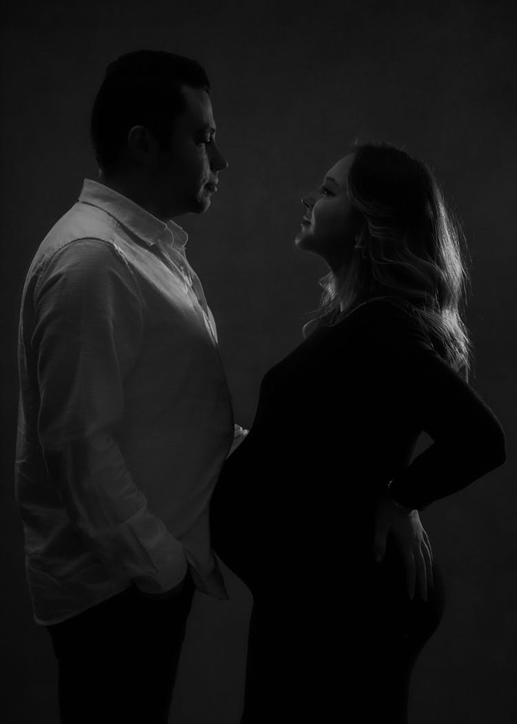 Black And White Shot Of A Husband And A Pregnant Wife Standing Face To Face 