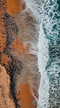 Stunning aerial view of ocean waves crashing on the sandy shore of Oceanside, CA, showcasing vibrant colors and textures.