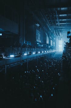 Dimly lit indoor concert scene with audience holding glowing cellphones.