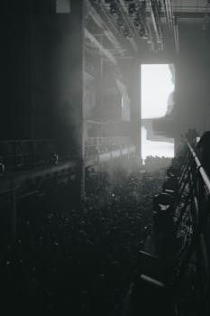 A foggy industrial interior filled with a dense crowd, invoking an eerie and mysterious atmosphere.