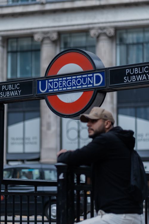 Free A man in a cap standing near the iconic London Underground sign on a city street. Stock Photo
