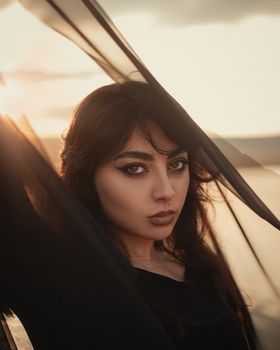 Captivating portrait of a woman posing with a veil at sunset, highlighting elegance and fashion.