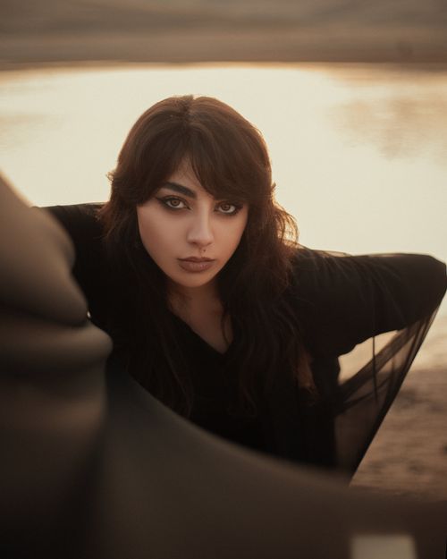 Free A striking portrait of an elegant woman posing by a serene lake at sunset, exuding beauty and style. Stock Photo
