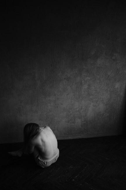 Fotomural Retrato artístico en blanco y negro de una mujer sentada contra una pared, mostrando un estado de ánimo sombrío.