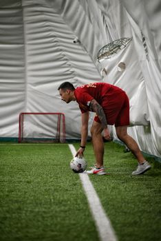 A man in red sportswear preparing for a soccer match indoors.