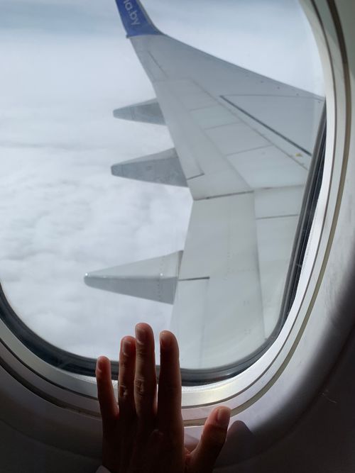 Free View from an airplane window showing a hand and the aircraft wing above the clouds. Stock Photo