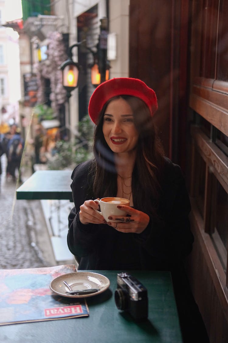 Fashionable Woman In A Black Coat And Red Beret Drinking Coffee