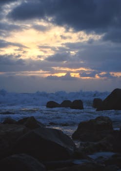 Captivating view of the dramatic sunset over Alexandria's rocky coastline with crashing waves.