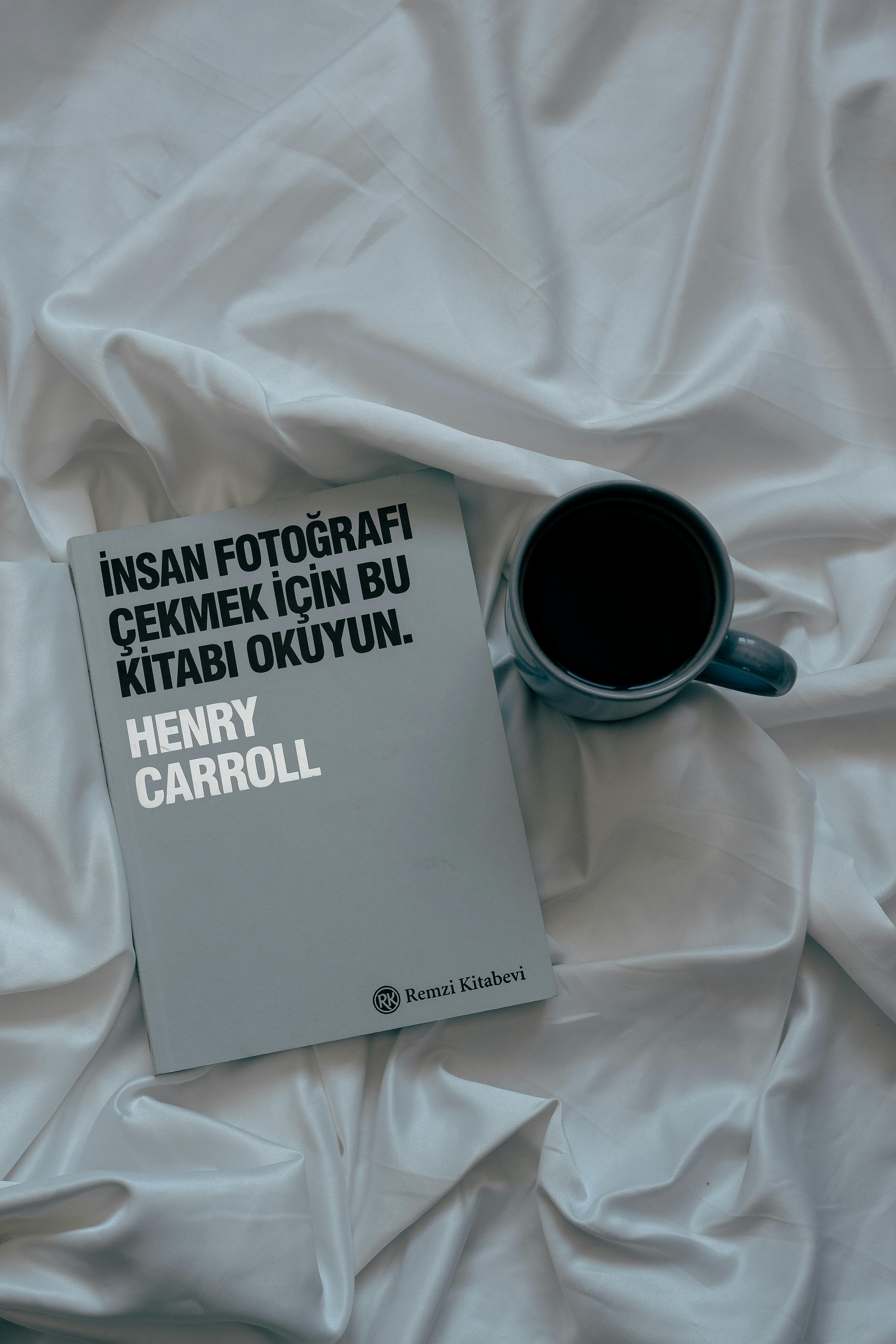 A sleek book and coffee cup on white fabric create a sophisticated flat lay capture.