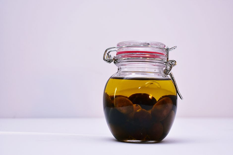 A glass jar containing olives submerged in oil with a sealed lid on a white background.