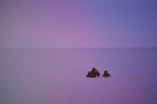 Free Two divers silhouetted against a vibrant sky at dusk in the calm ocean waters, creating a serene and adventurous vibe. Stock Photo