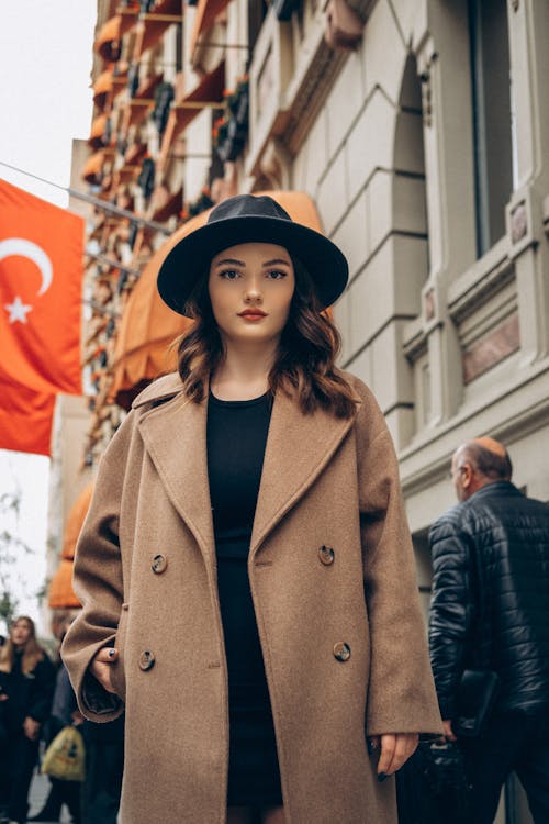 Woman in Camel Coat and Fedora Hat Standing on Street