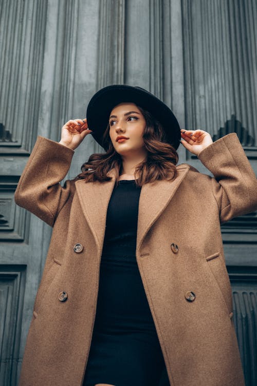 Young Elegant Woman in a Brown Coat and a Hat Posing in front of Antique Door 