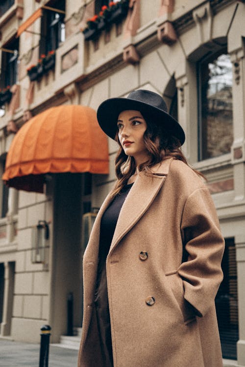 Young Elegant Woman in a Brown Coat and a Hat Posing in City 