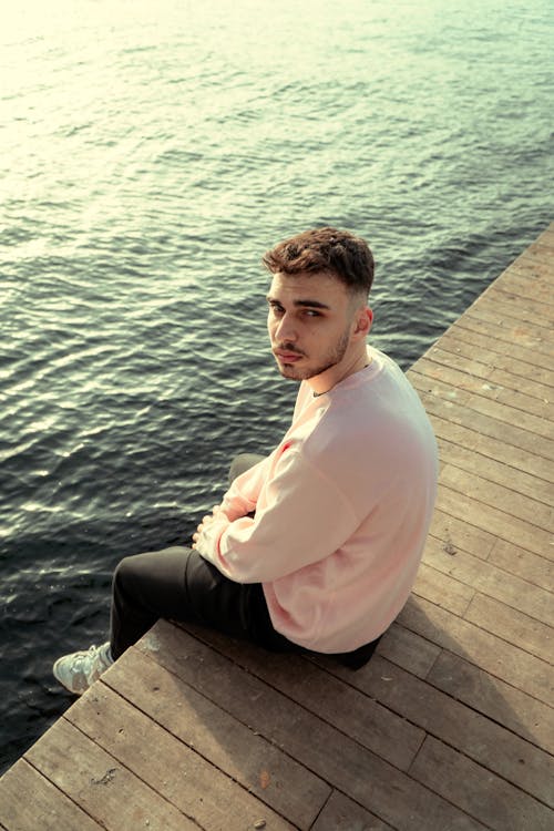 Free Young Man Sitting on a Wooden Pier  Stock Photo