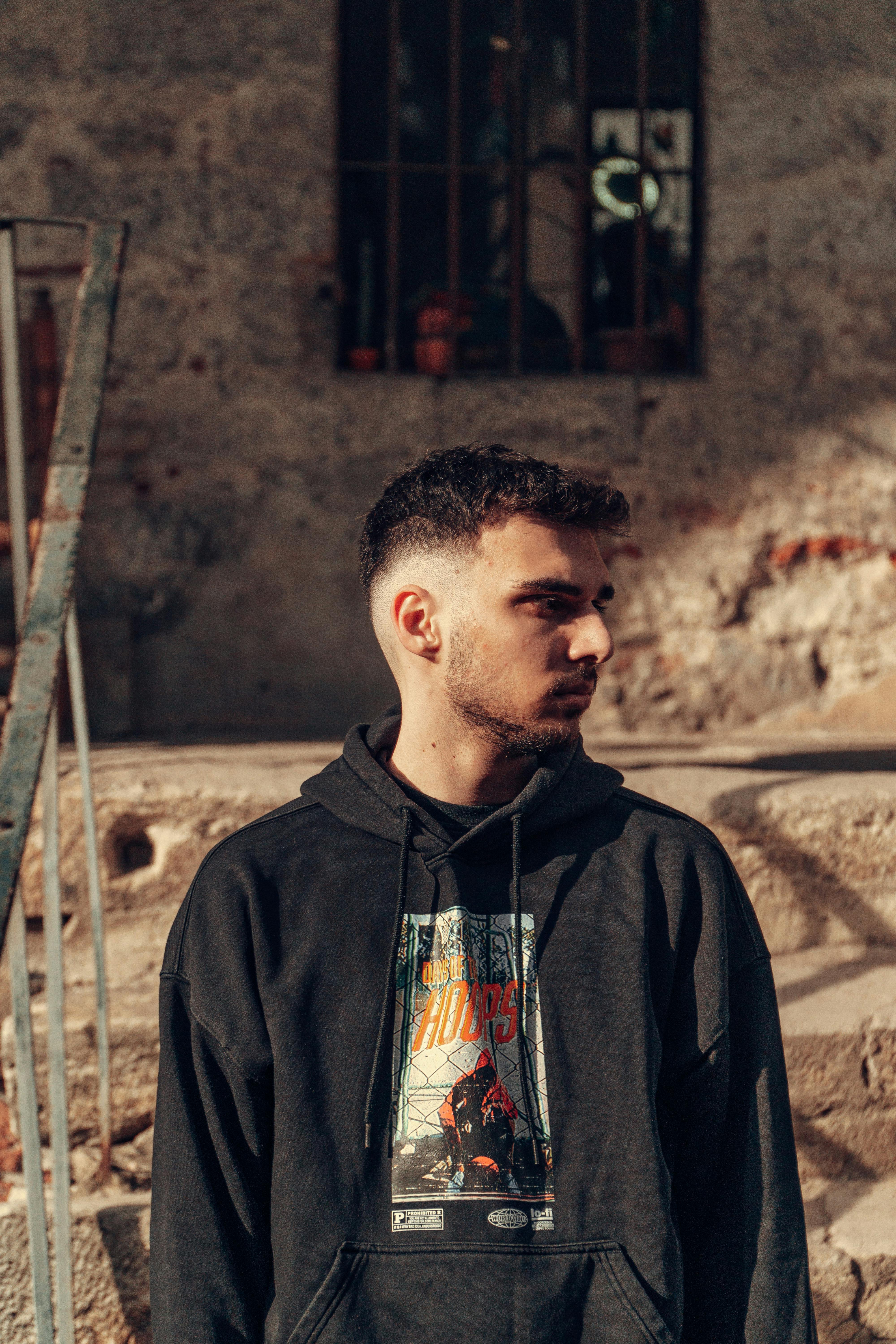 Stylish young man wearing a graphic hoodie in an urban setting. Warm lighting and casual vibe.